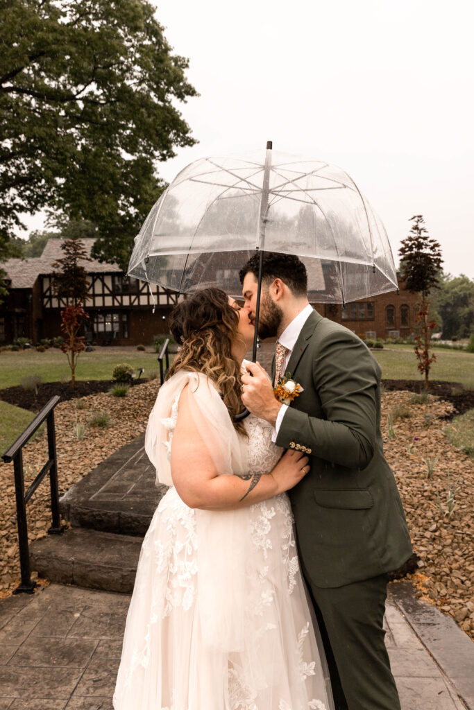 Bride and groom under umbrella during rainy Tudor House wedding on Portage Lakes