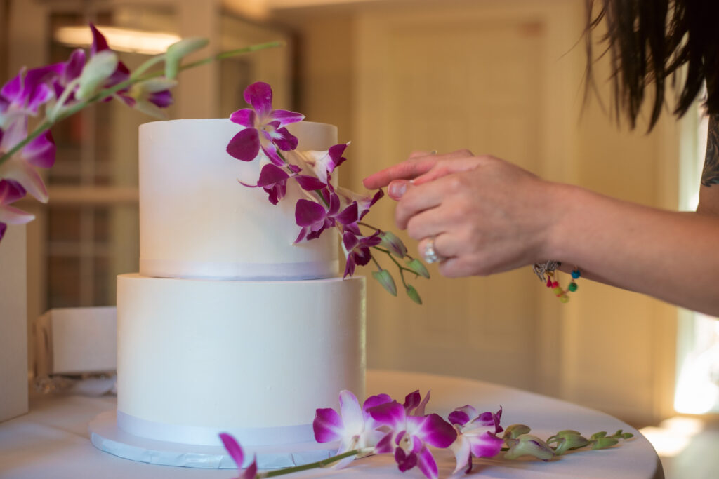 Baker placing orchids on a wedding cake during reception setup in Northeast Ohio