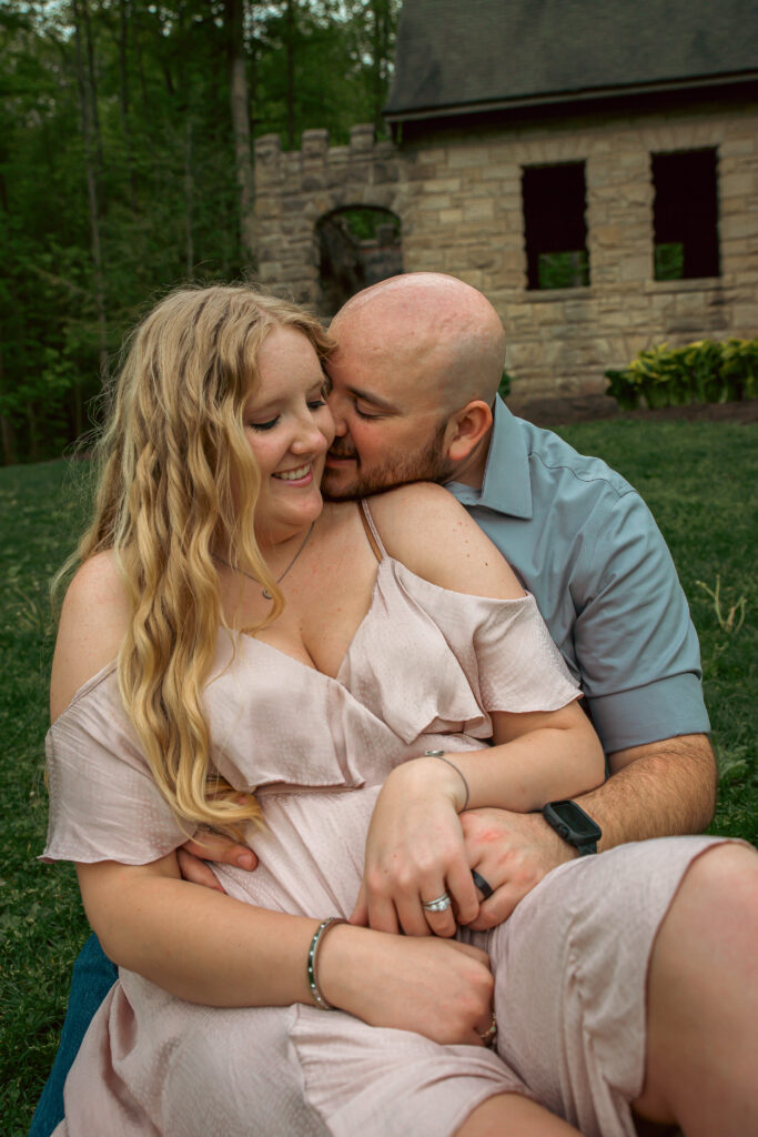 Cozy engagement photo of couple cuddling on the grass in front of Squire’s Castle near Cleveland.