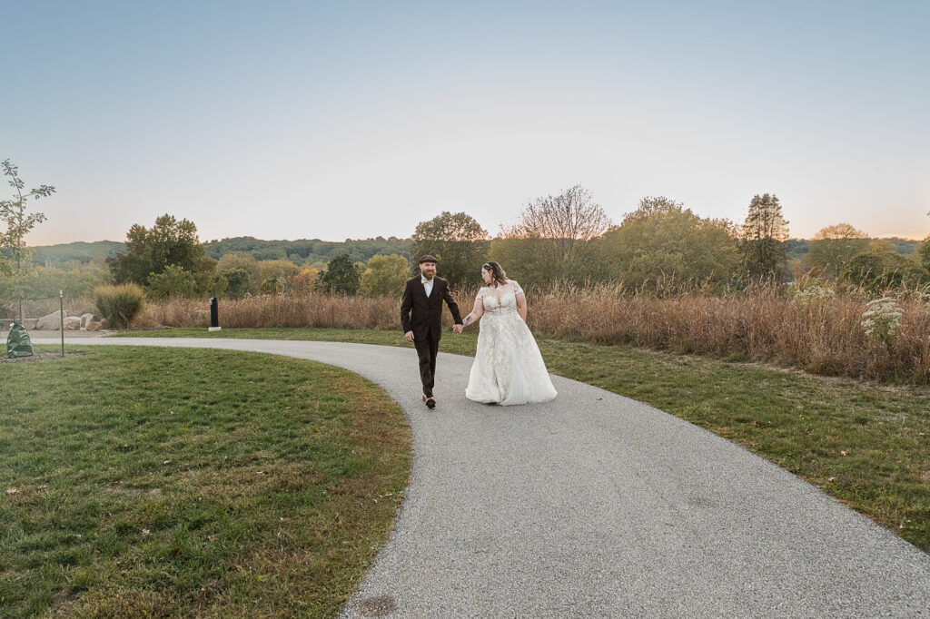 Bride and groom walking along the paved path at Cascade Valley Metro Park with fall colors in the background