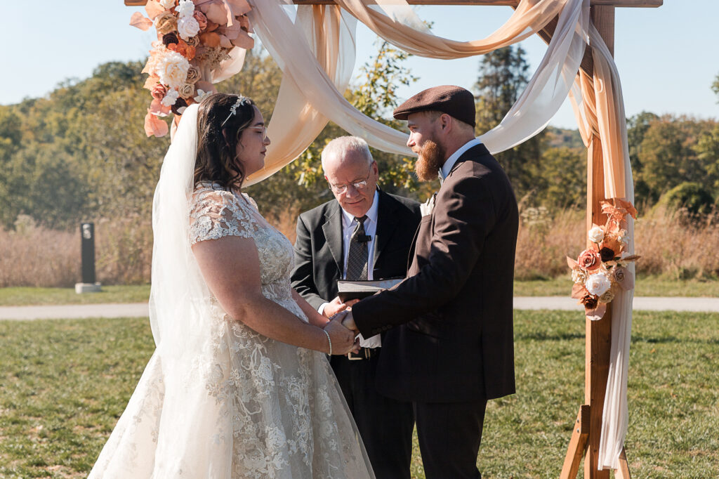 Outdoor wedding vows beneath a decorated arch on the grassy ceremony space at Himelright Lodge in Cascade Valley Metro Park
